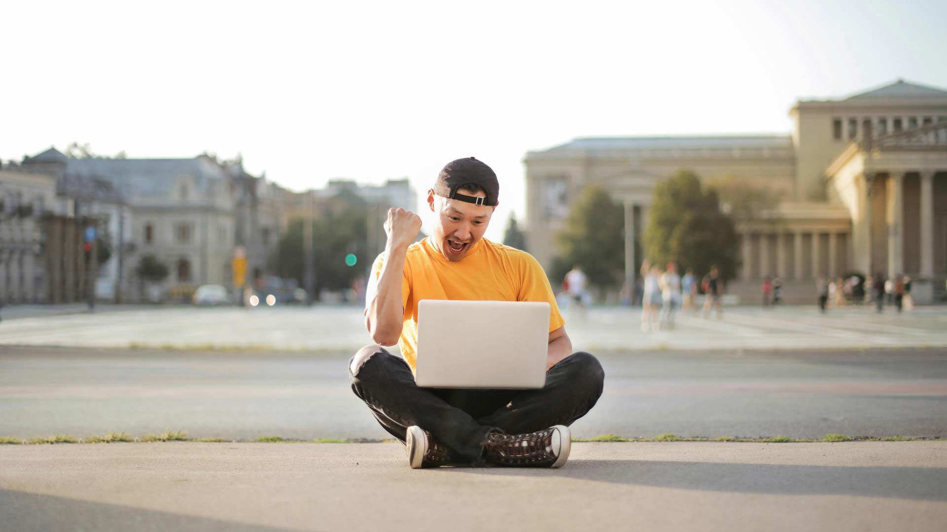 A person sitting outdoors with a laptop, celebrating success, symbolising location-based personalisation where content is tailored based on the user's geographical context.