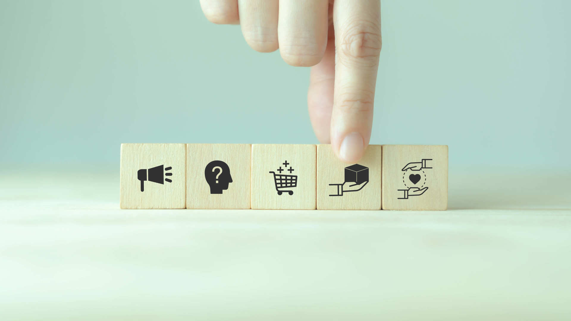 A hand placing a wooden block on the table representing customer purchasing journey.