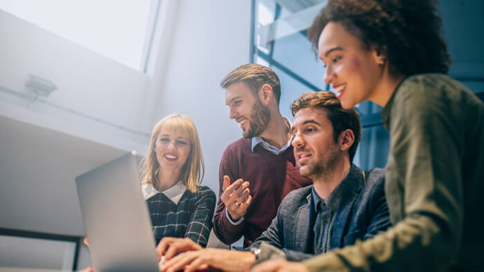 A group of people are looking at the laptop on the table.