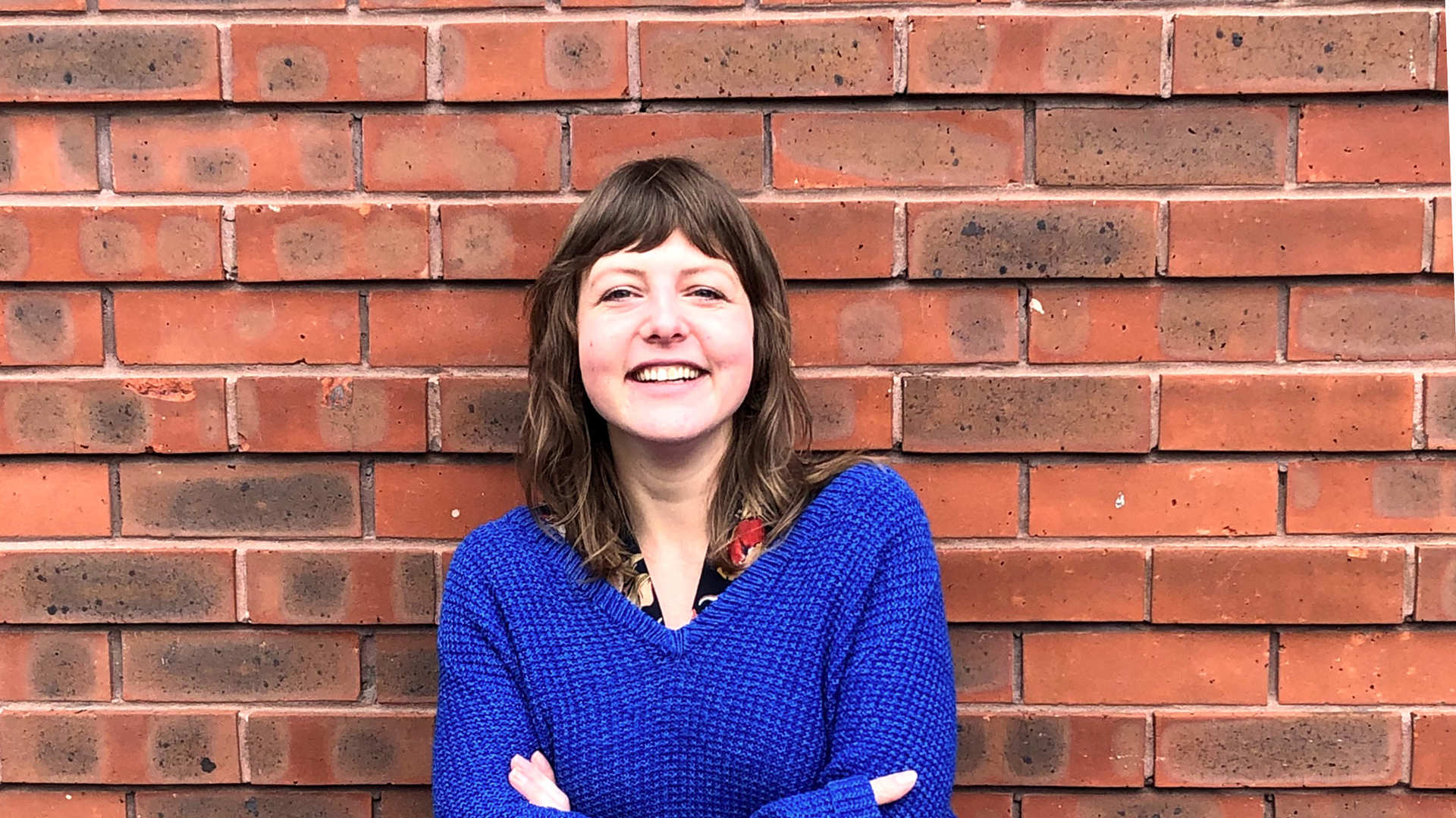 Smiling female is standing next to the brick wall