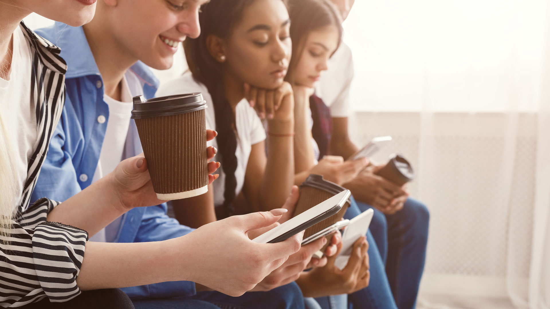 Teenagers group sitting in a row and holding phones