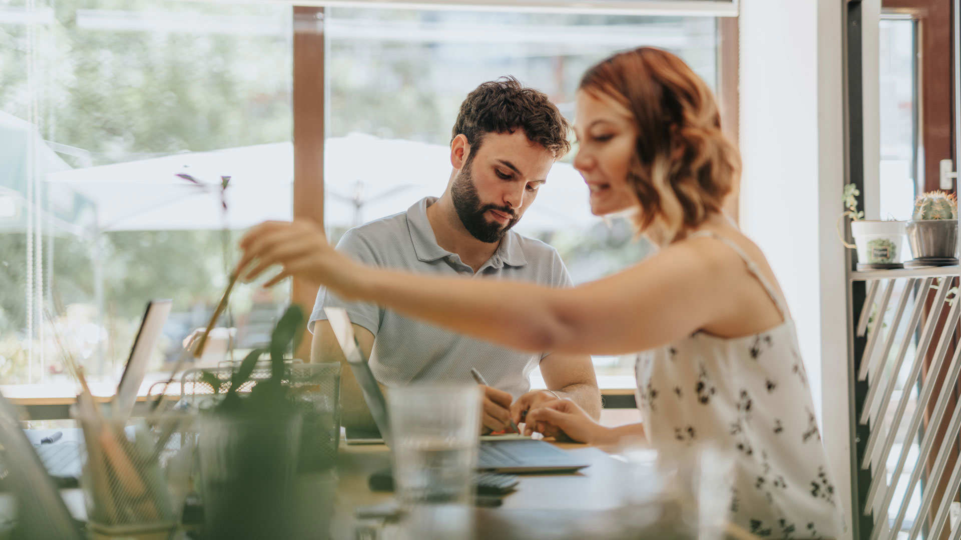 Two people collaborating at a table with digital tablets and art supplies, representing behavioural data collection through user interaction for personalised website experiences.