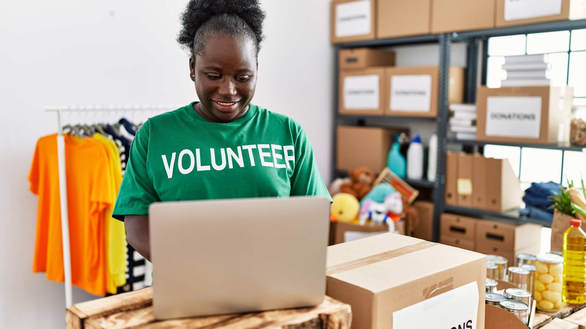 Women with volunteer t shirt is standing next to the open laptop in the middle of the charity shop